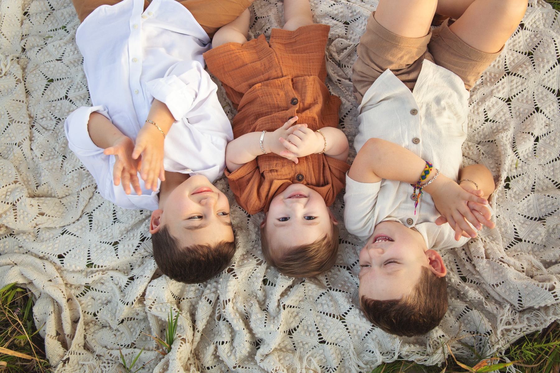 three boys lay on their backs on a vintage white blanket