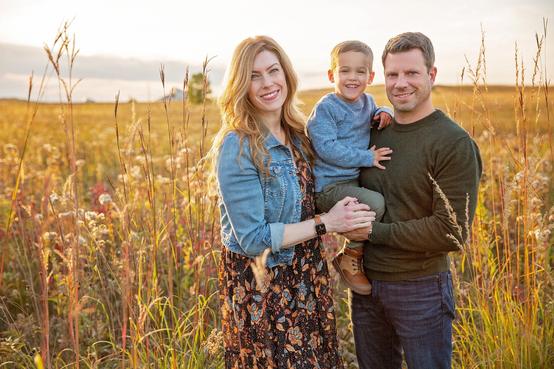 couple with young boy in their arms in a fall grassy field