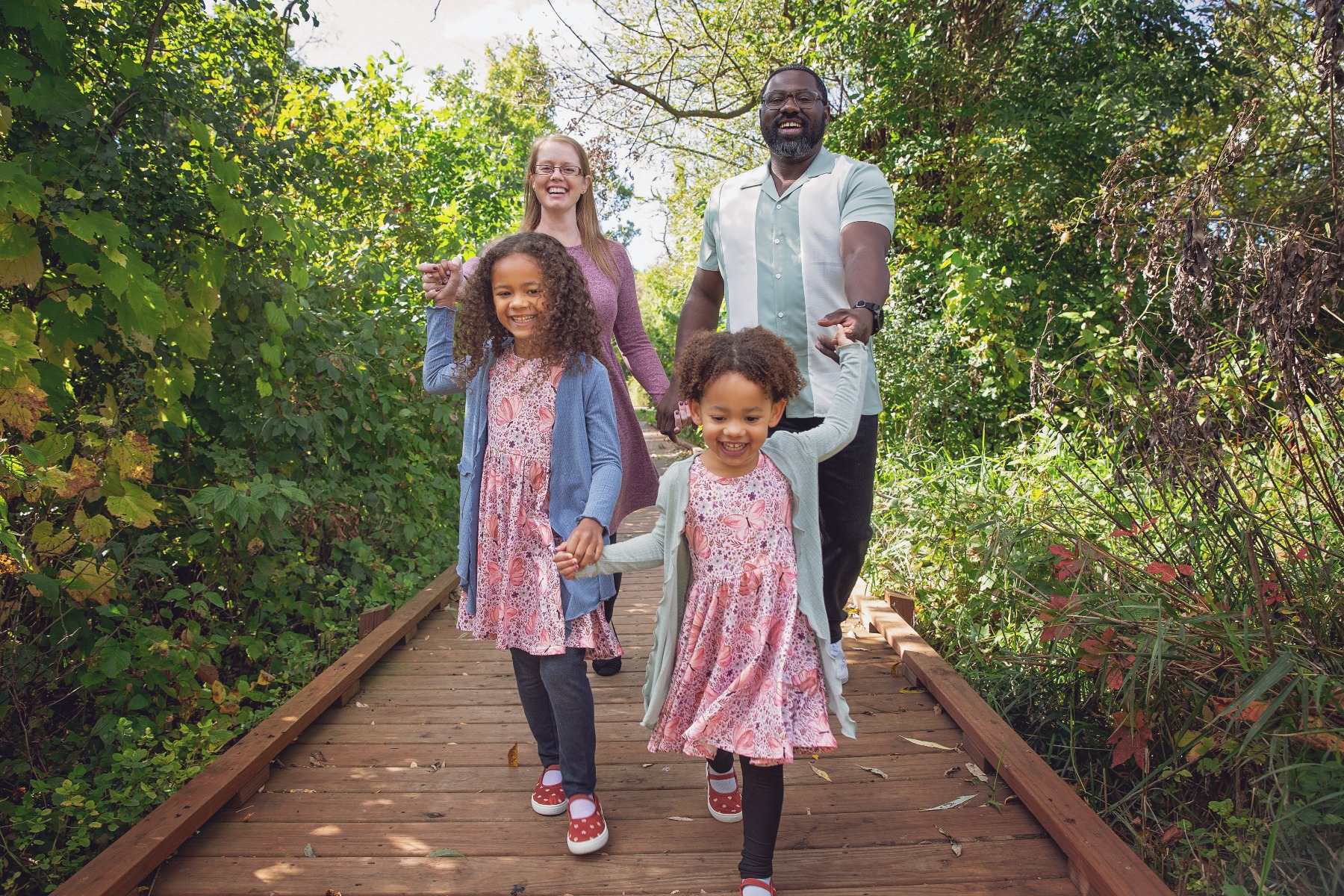 two curly haired girls laugh as they pulling their parents along on a wooden boardwalk
