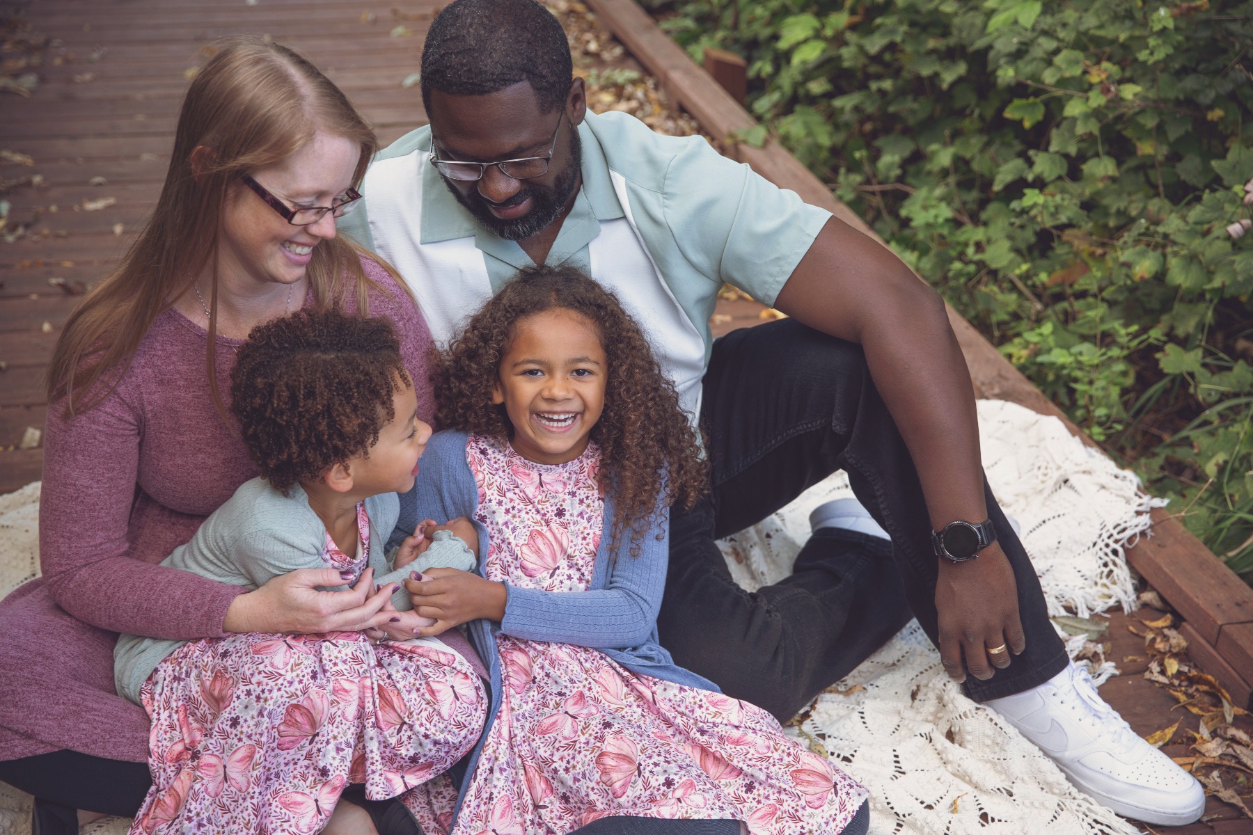 family of 4, two girls with curly hair snuggle in their parents lap