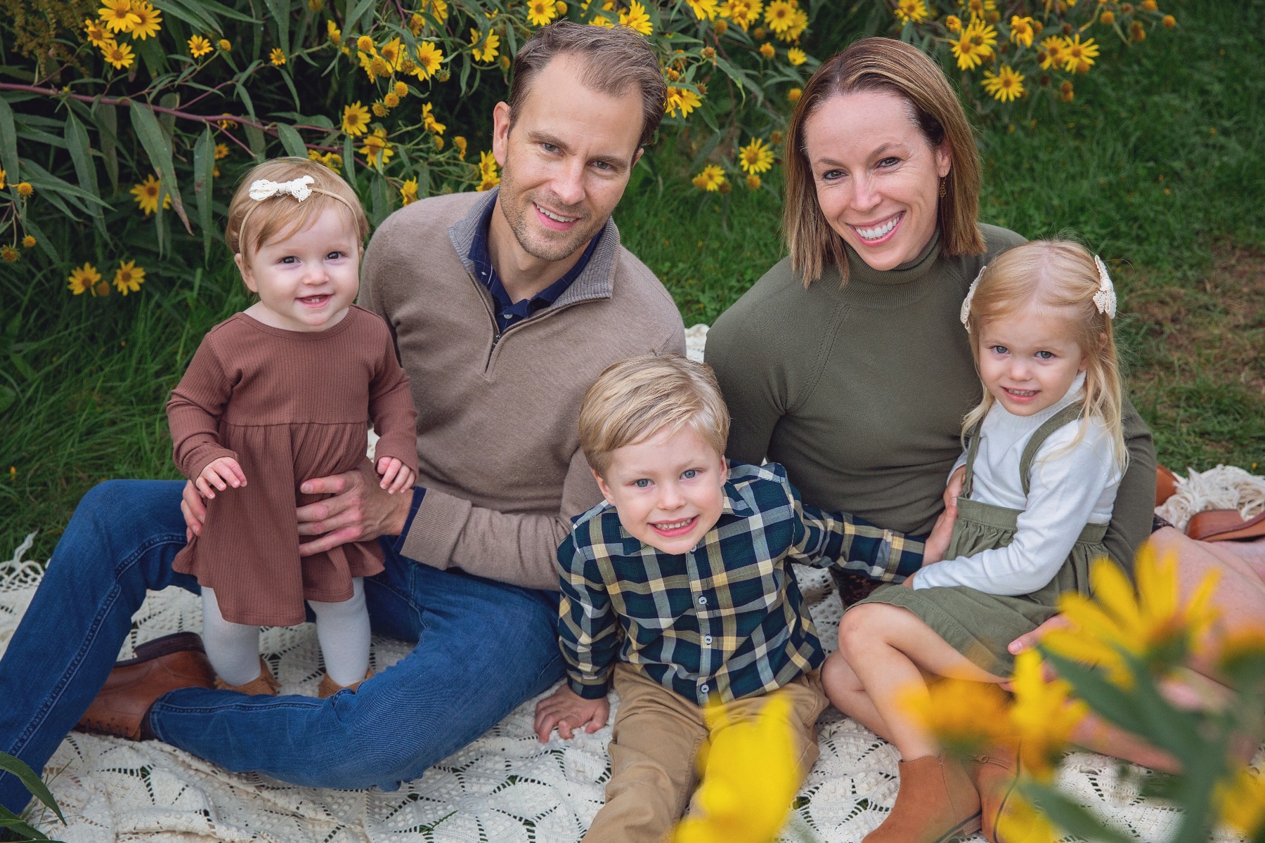family of 5 snuggle on a blanket amongst a field of yellow flowers