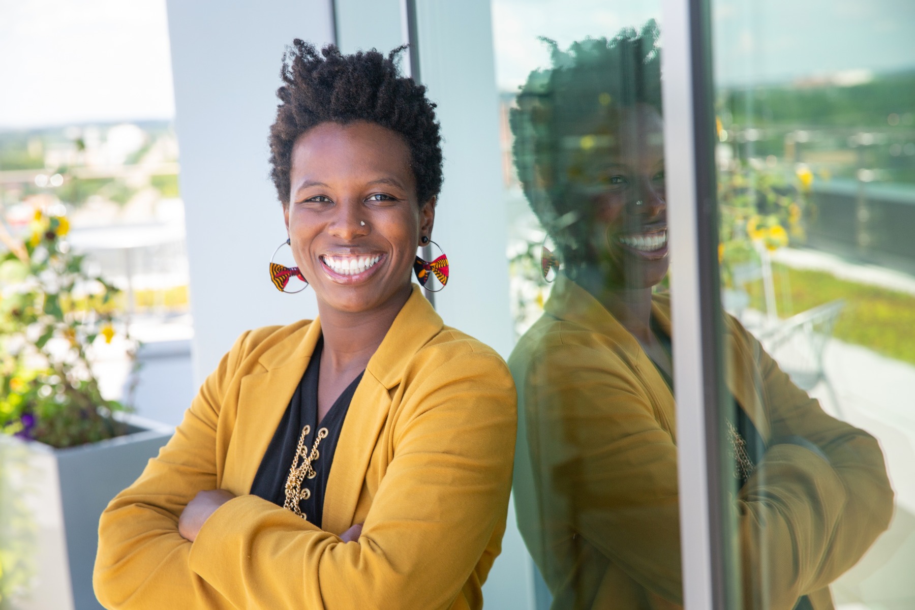 business woman in a yellow blazer poses for a professional portrait against a glass window