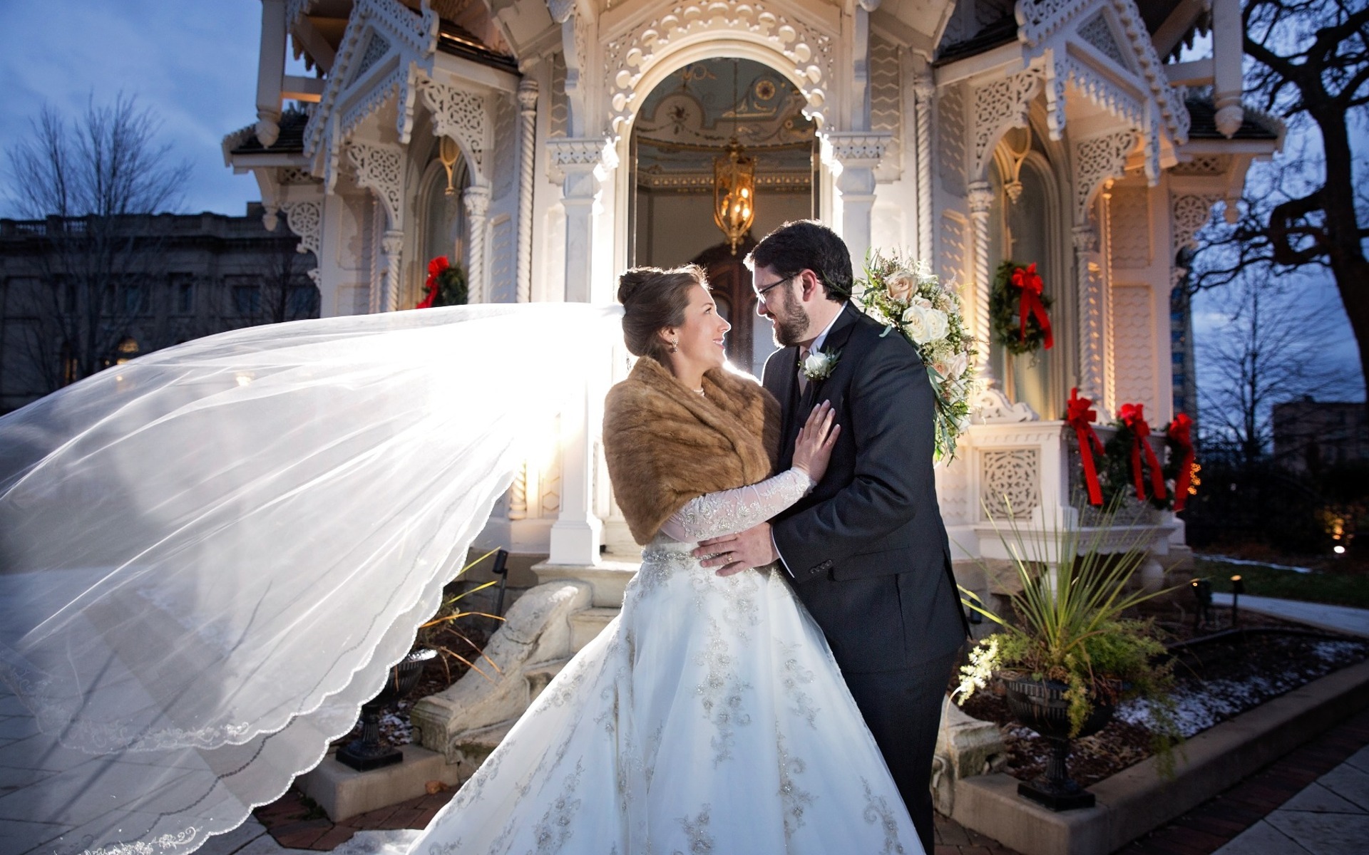 brides veil blows as she looks at groom, backlit at night