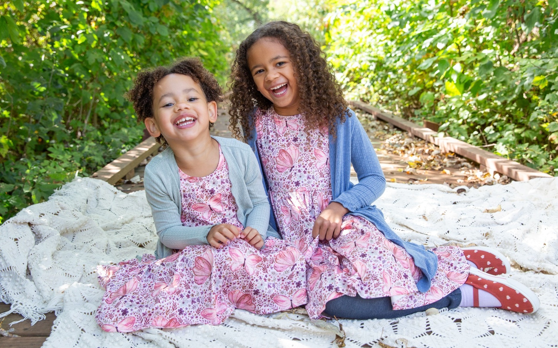 two girls in purple dresses laugh on a wooden boardwalk