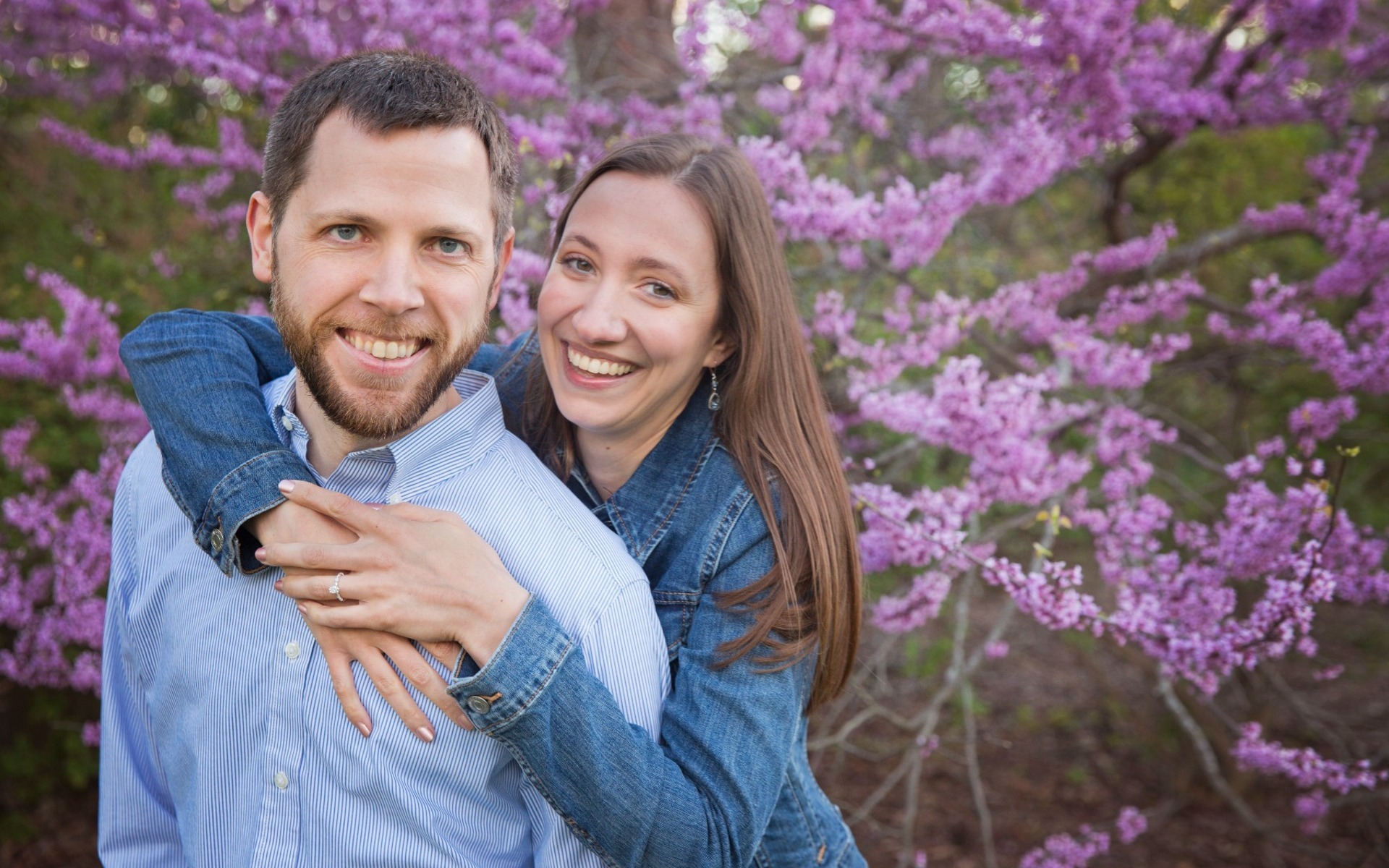 woman embraces a man from behind amongst spring blossoms