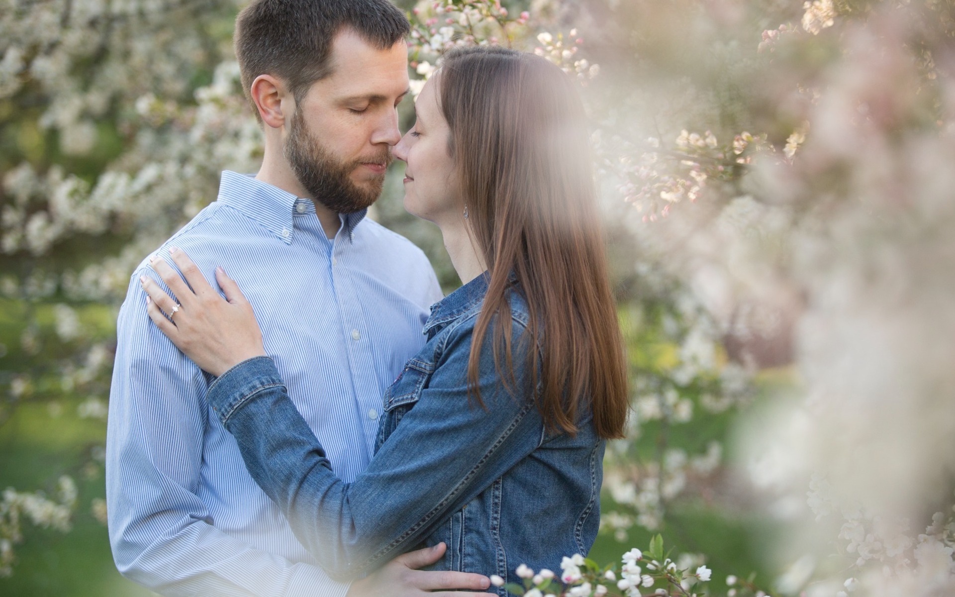 man & woman snuggle amongst white spring blossoms