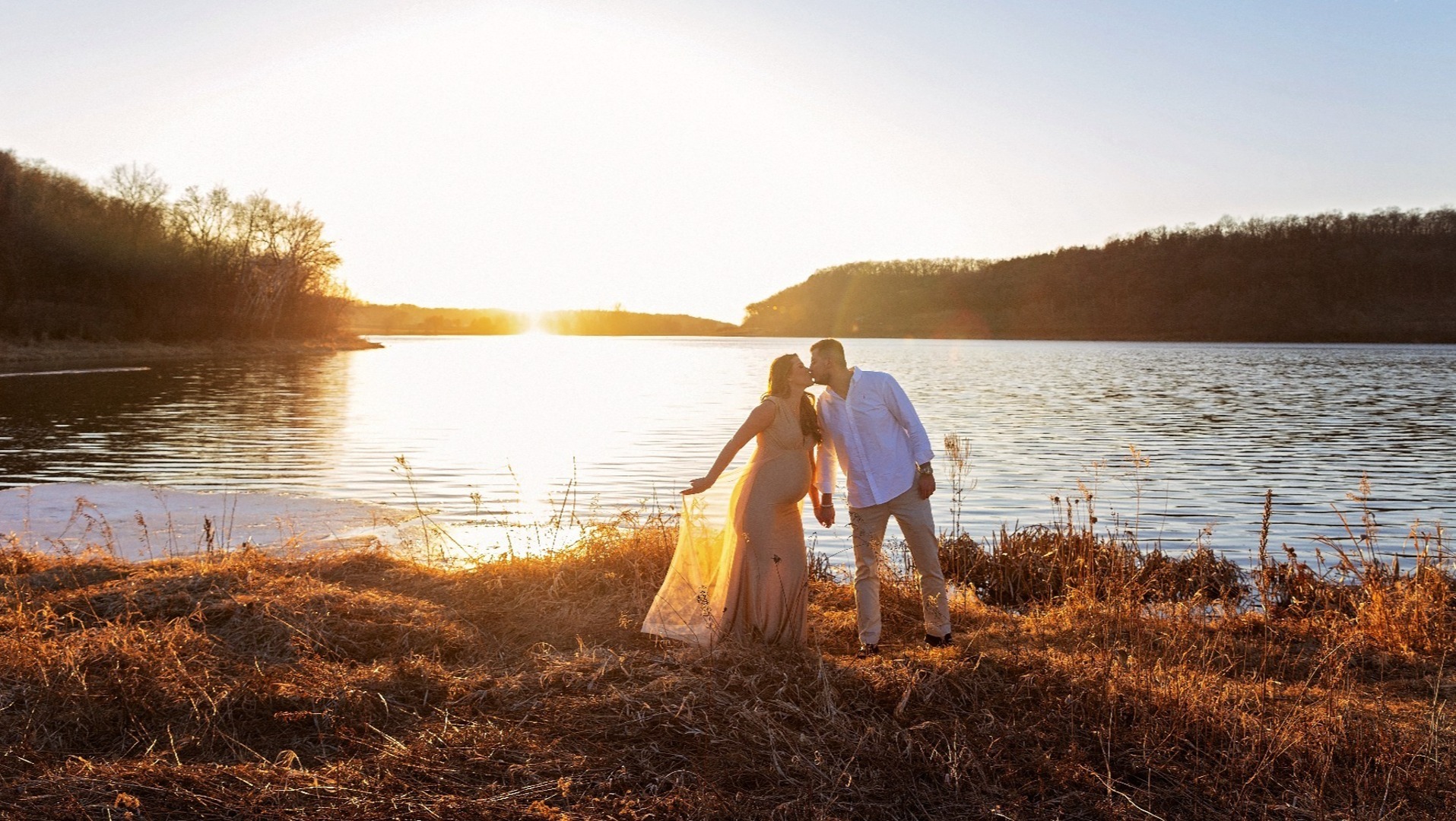 expectant mom & dad kiss in front of a sunset lake
