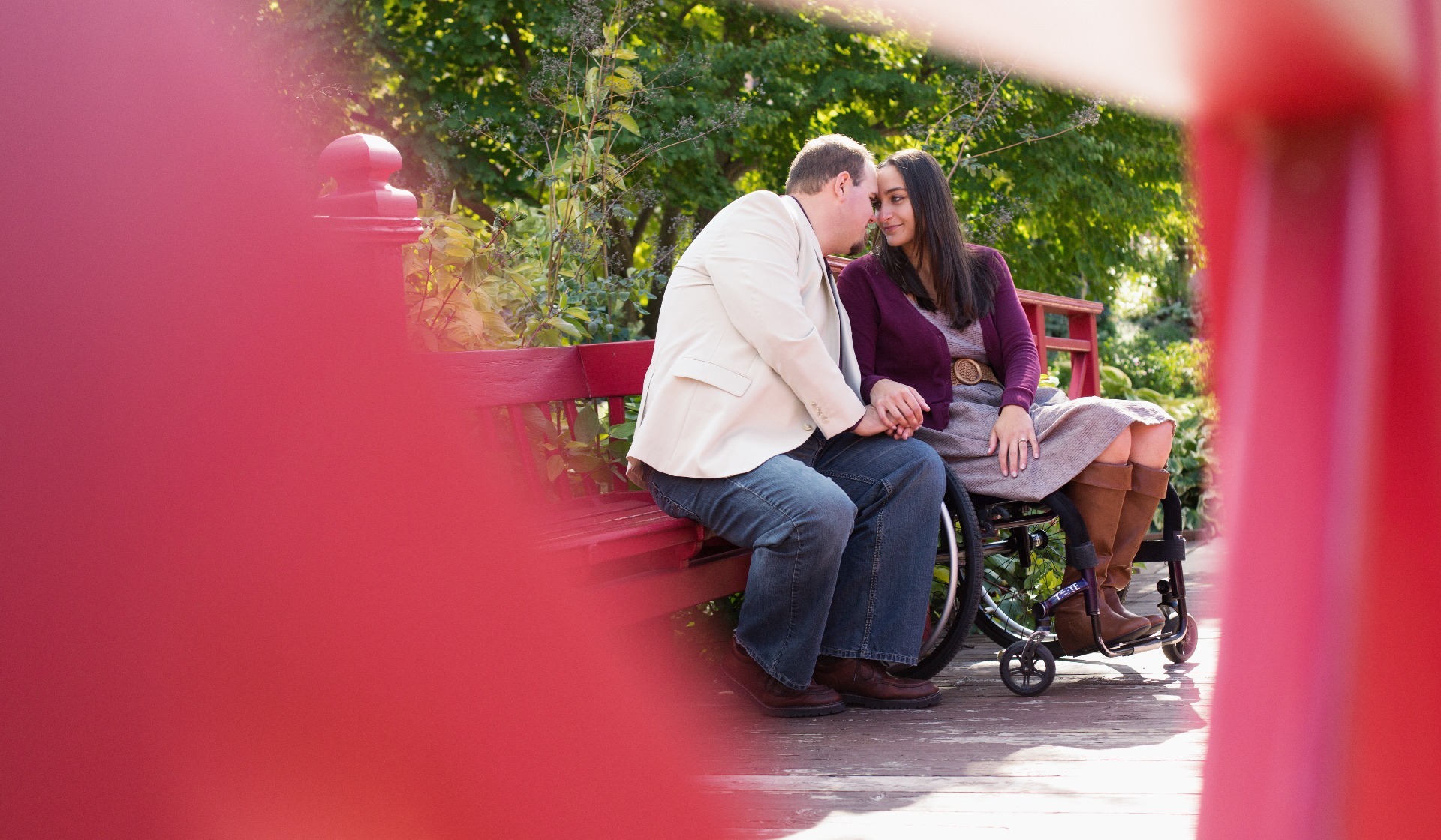 engaged couple sit together on a red bridge