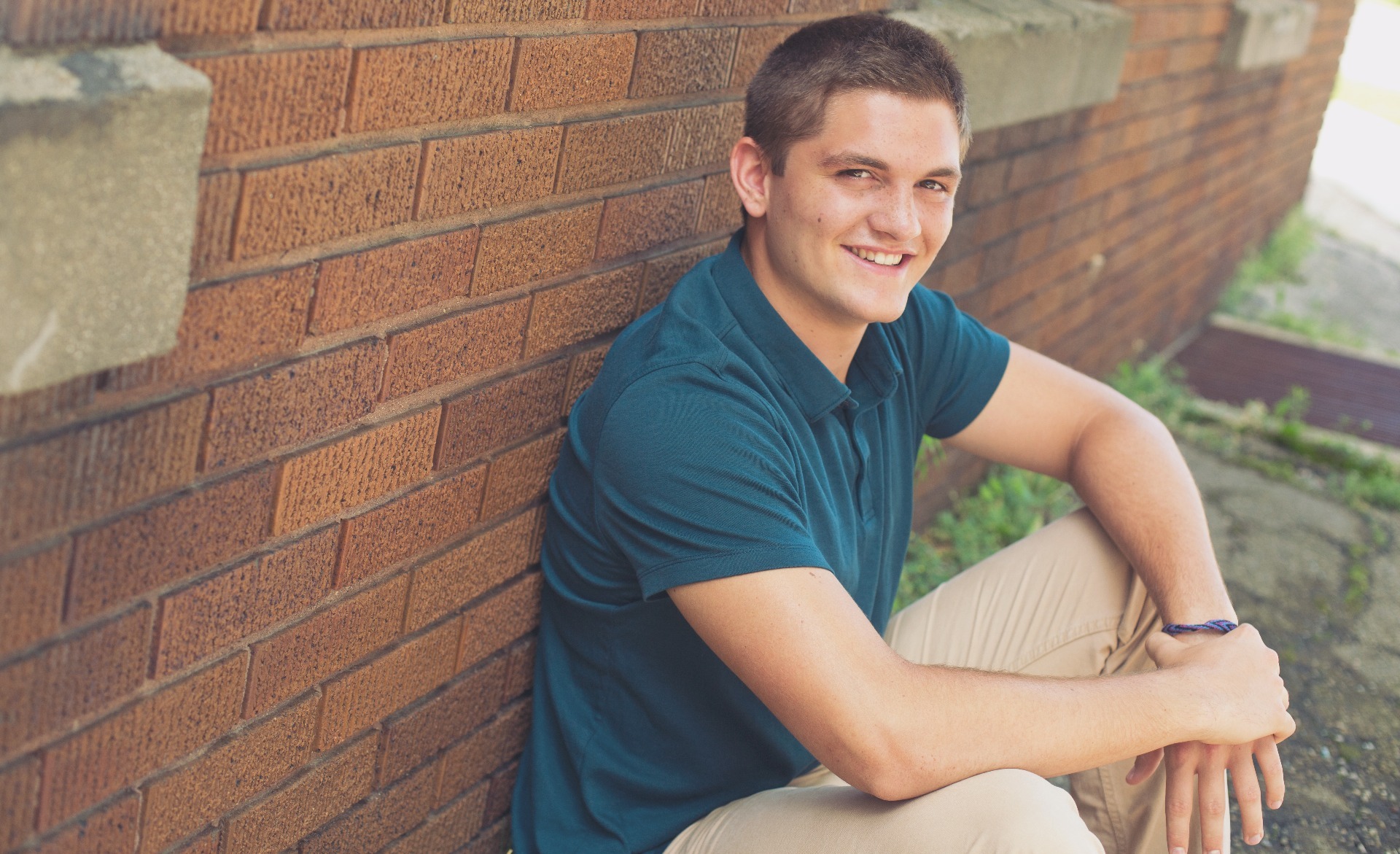 hs senior boy sits against a brick wall