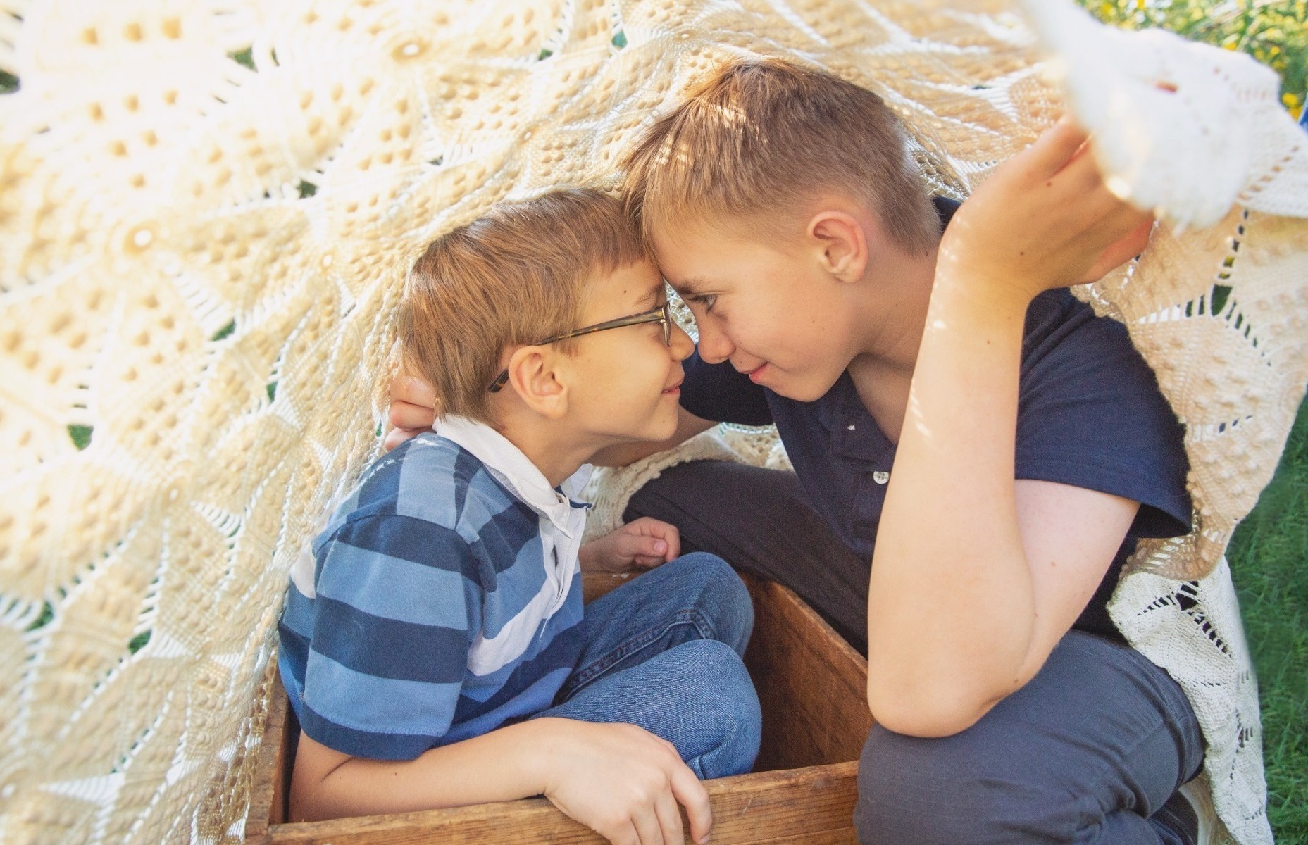 two boys play beneath a white blanket