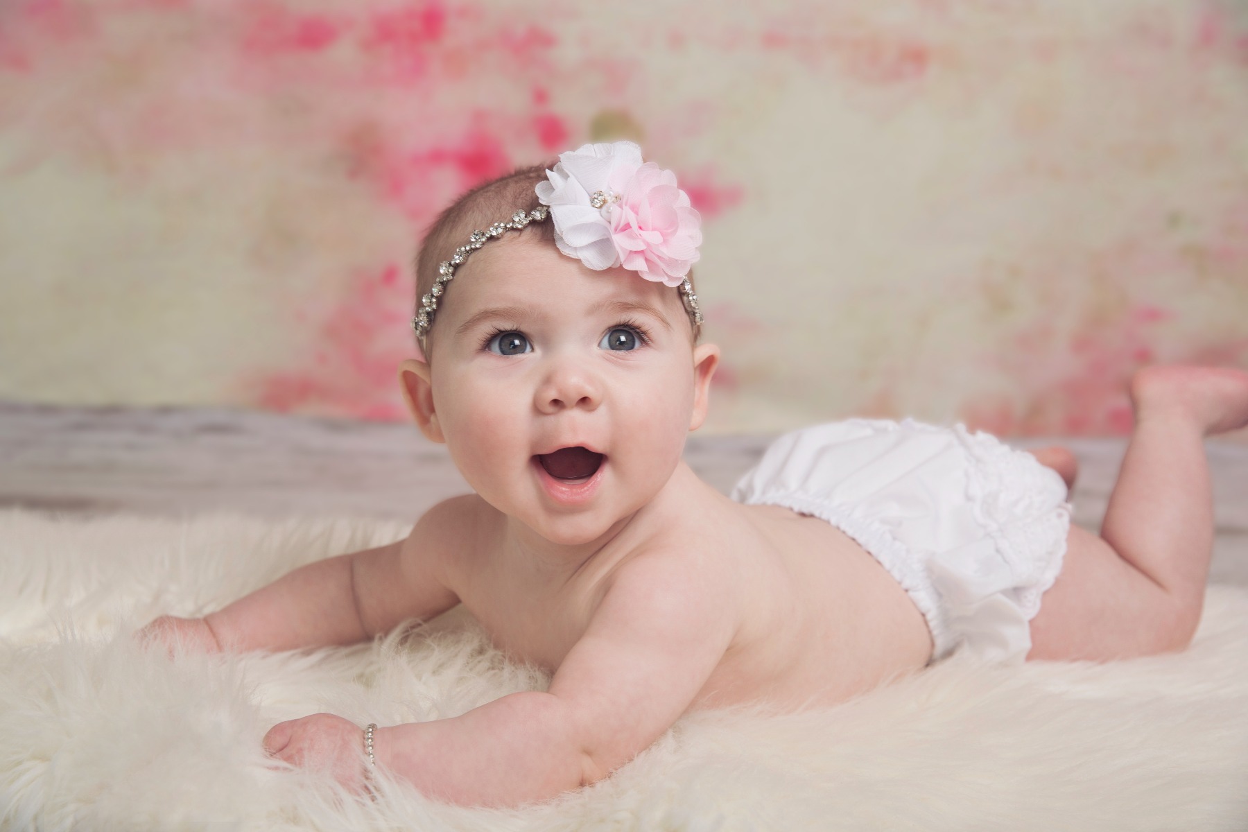 8 month baby on a white fur rug smiles