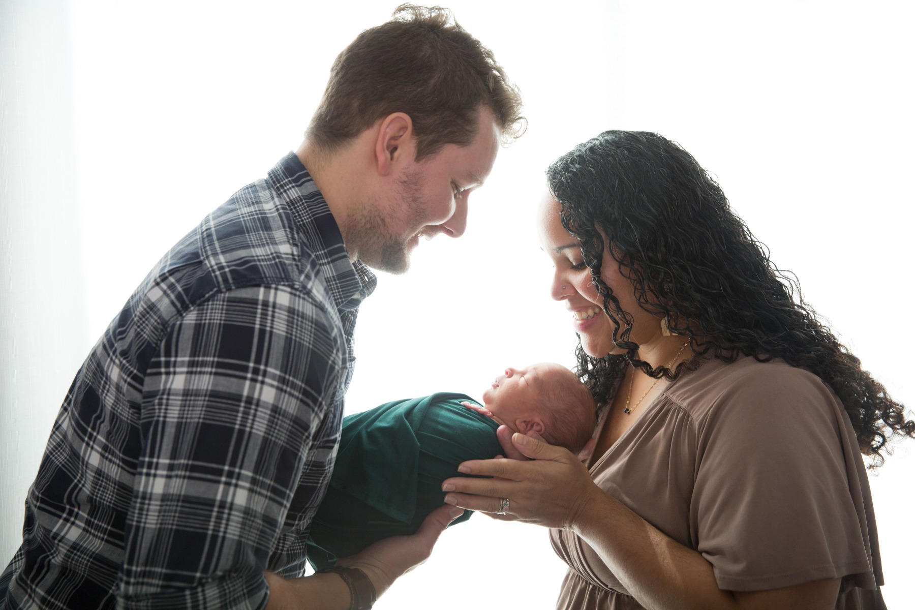 backlit mom & dad looking down at newborn baby
