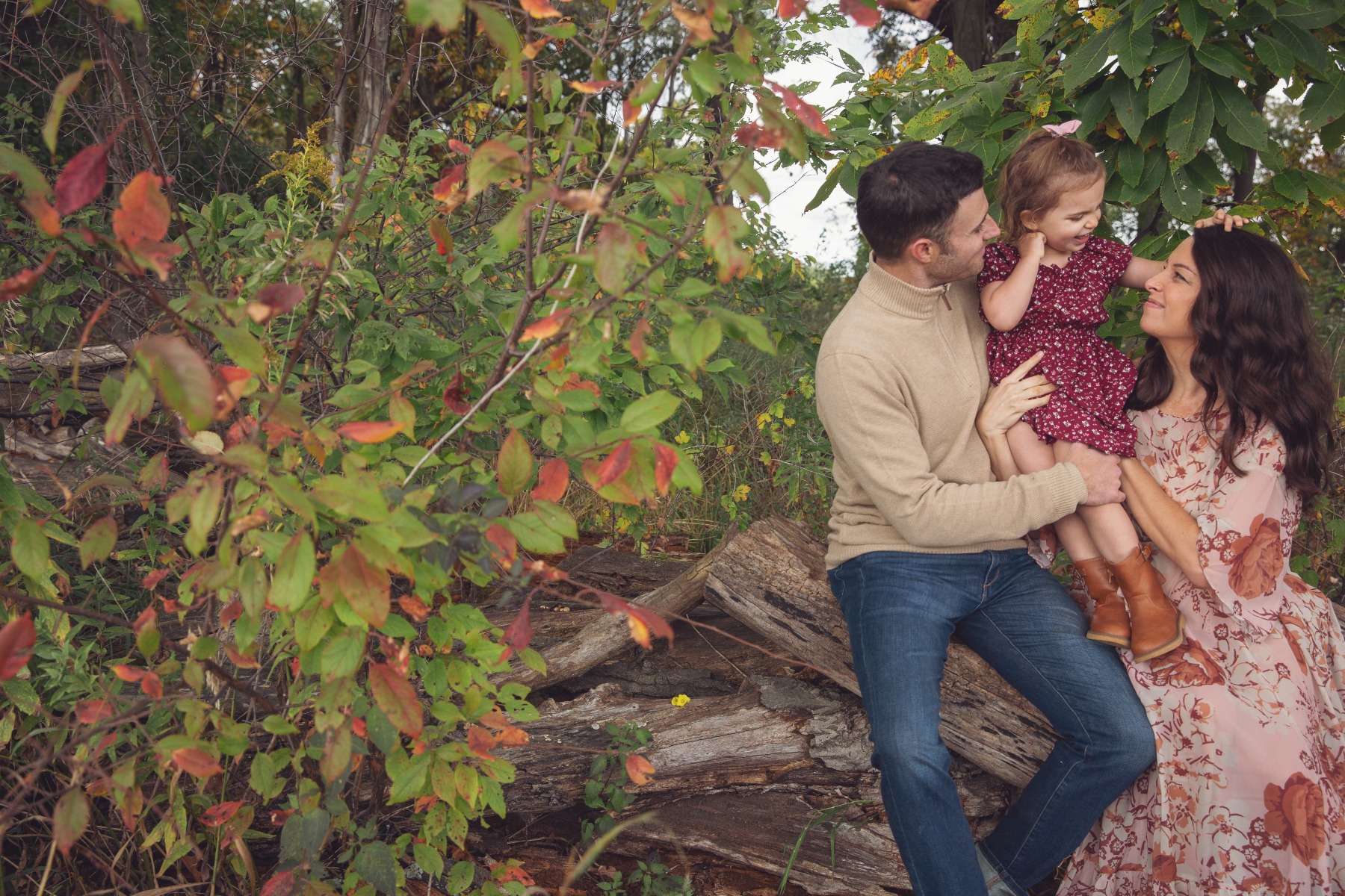 expectant mom & dad sit on a tree log with a little girl