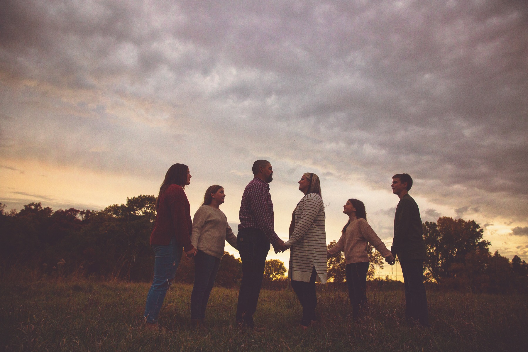 family of 6 hold hands silhouetted in front of a sunset