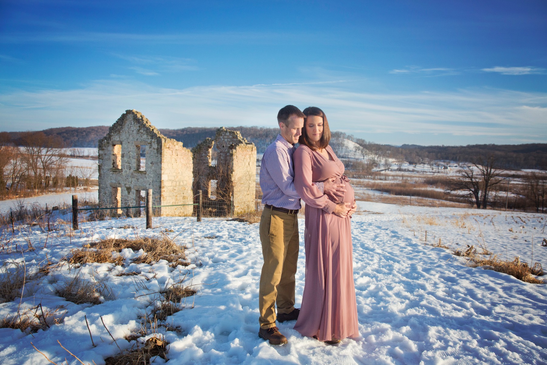 expectant mom & dad embrace on a snowy hillside