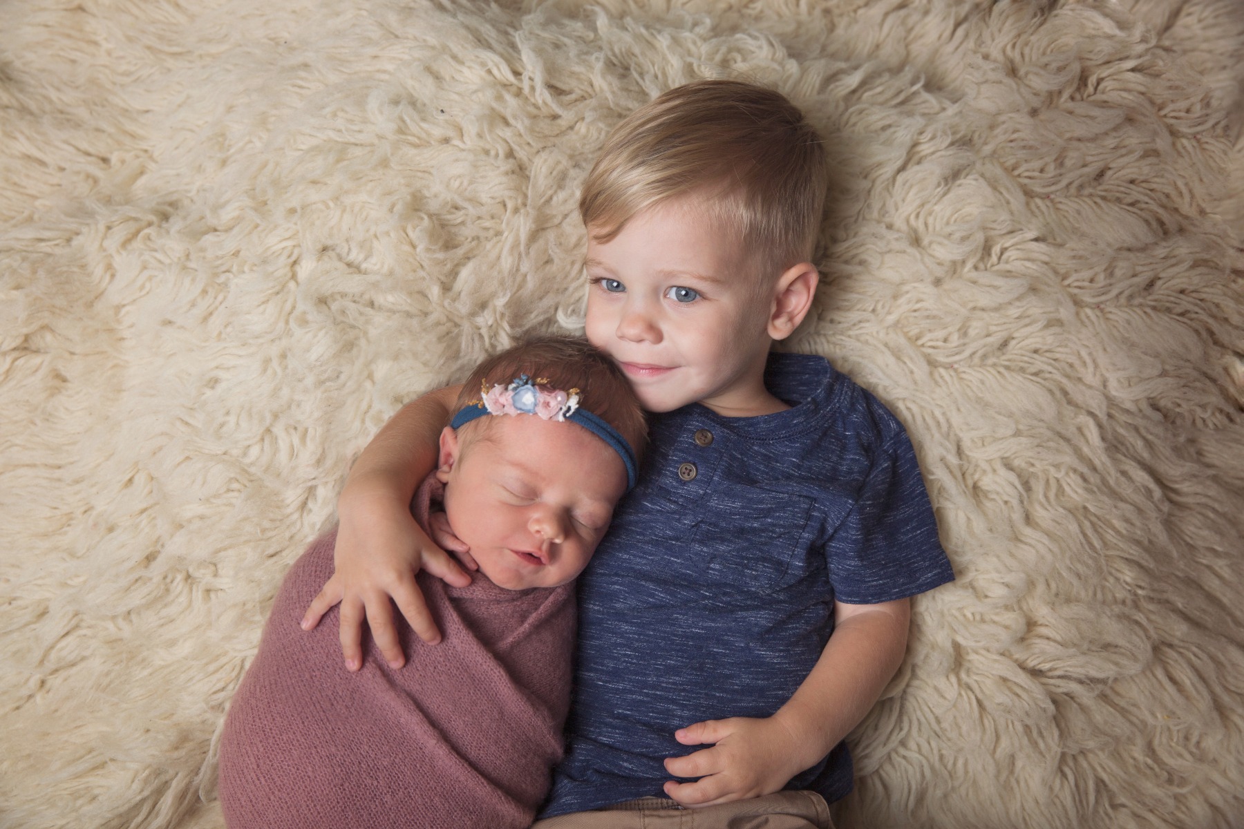 toddler boy snuggles his sleeping baby sister