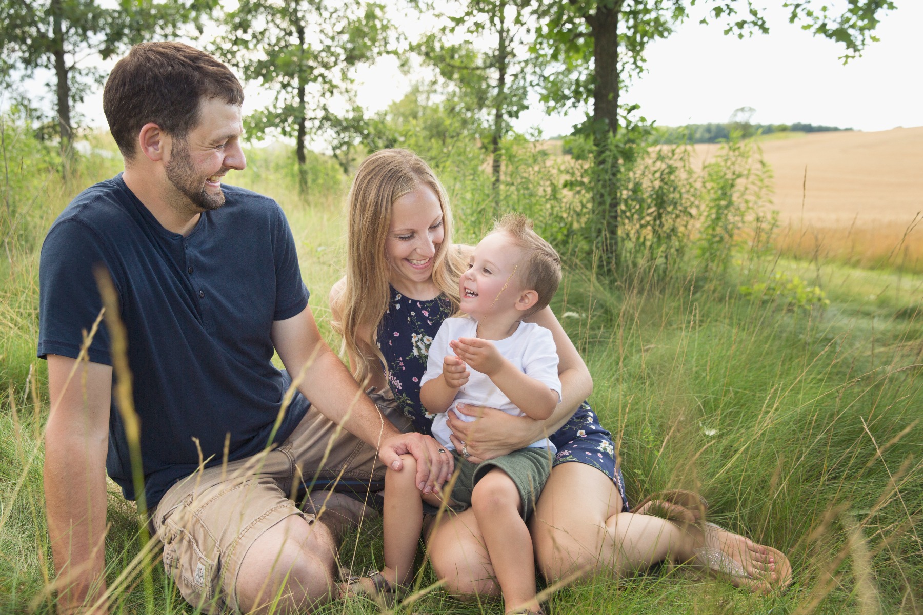 family of three laughs on a grassy hill