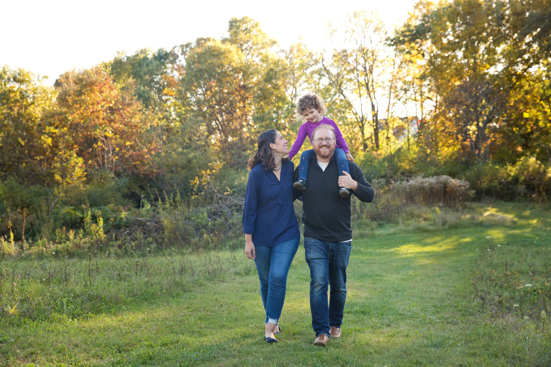 dad walks with daughter on his shoulders and mom by his side