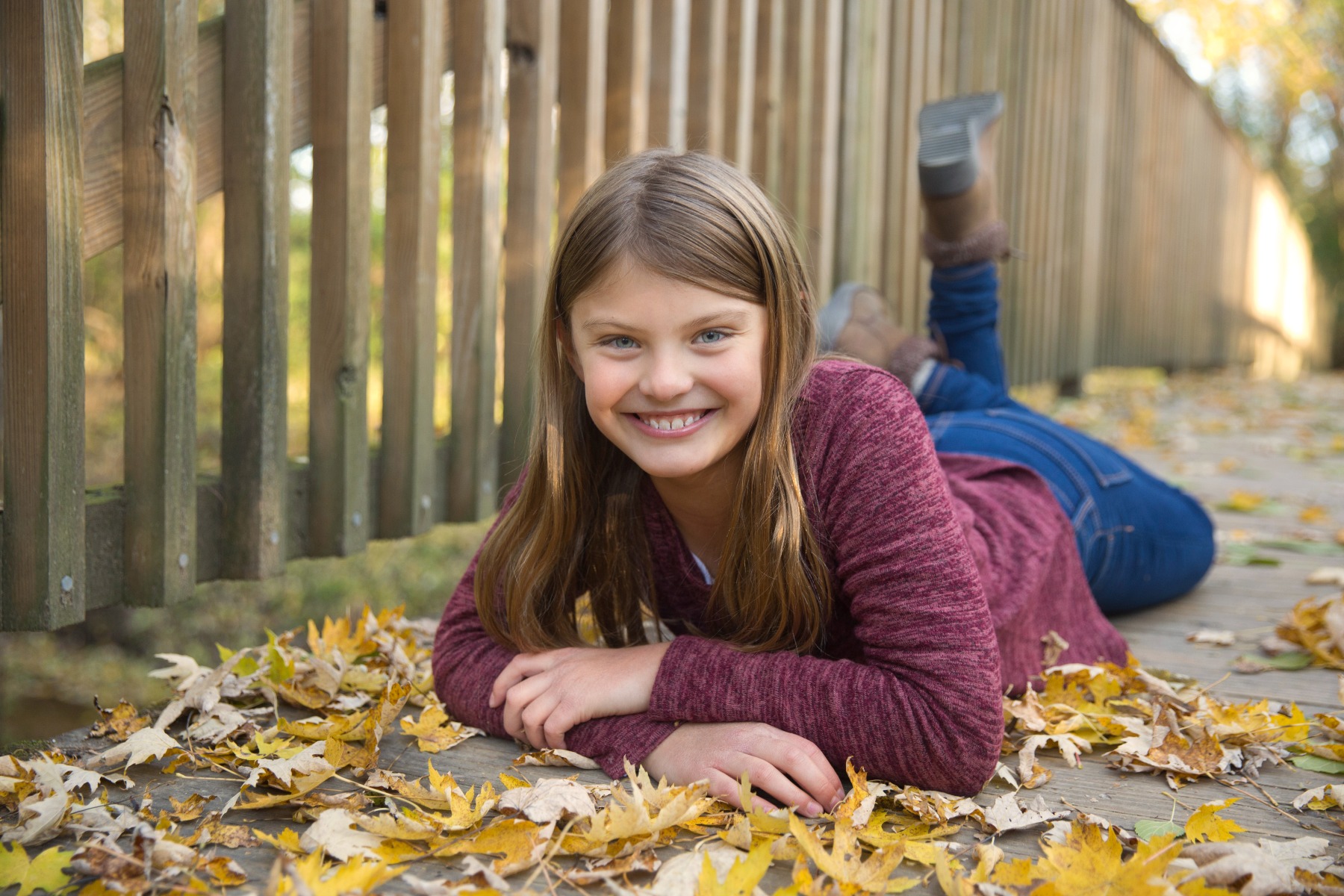 blond girl poses on her belly on a wooded bridge