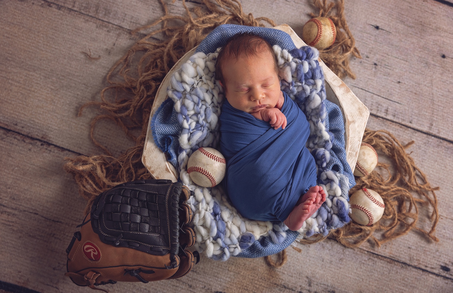 newborn baby boy sleeps in basket with baseball props all around