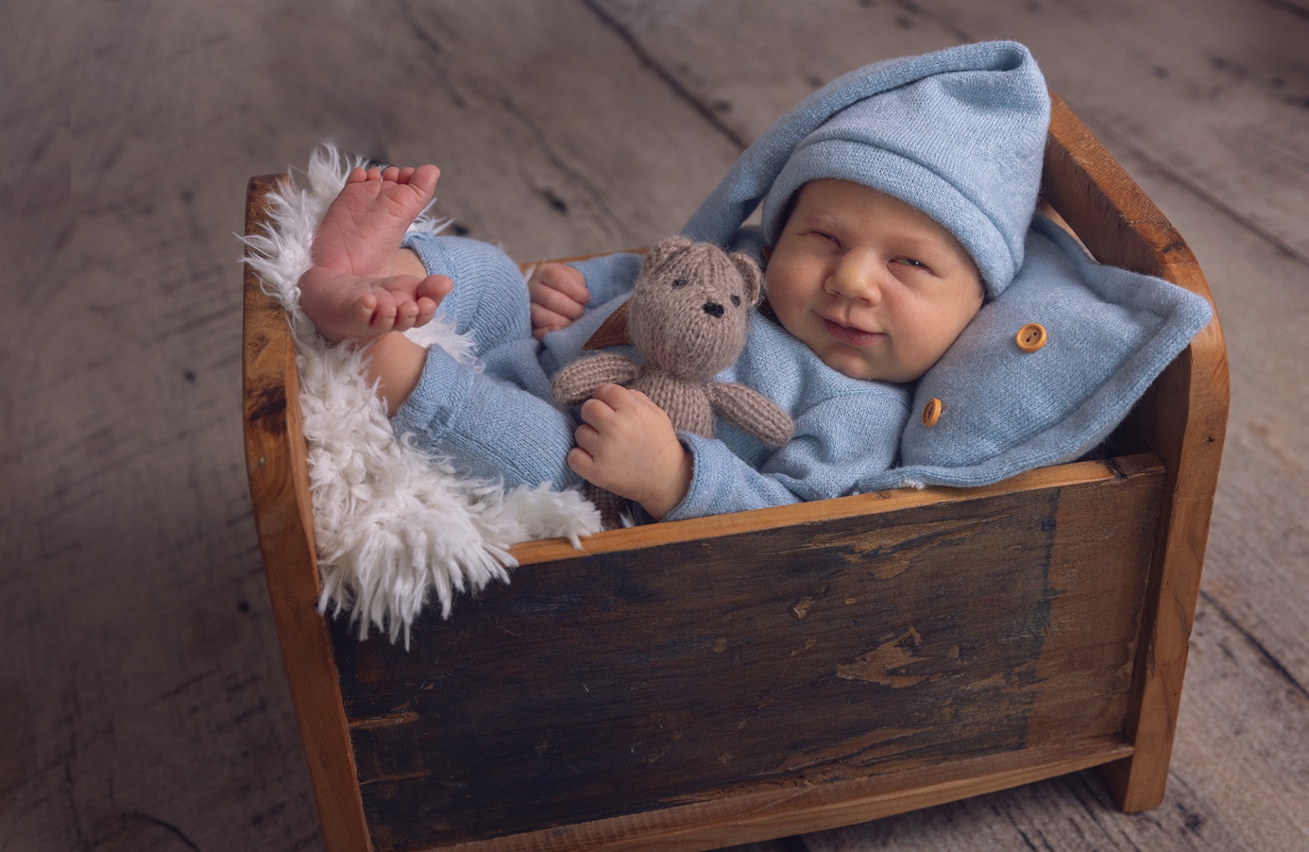 baby boy shares a sleepy smile from a wooden cradle