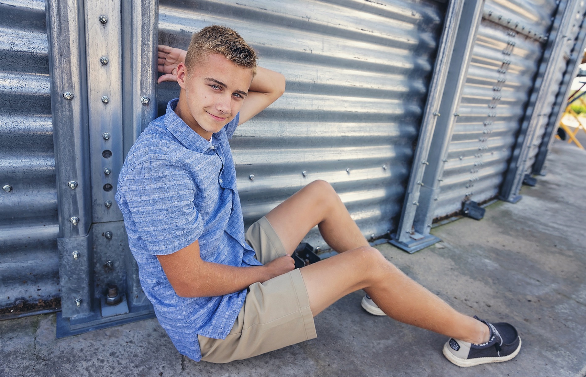 high school senior boy sits against a silver grain silo
