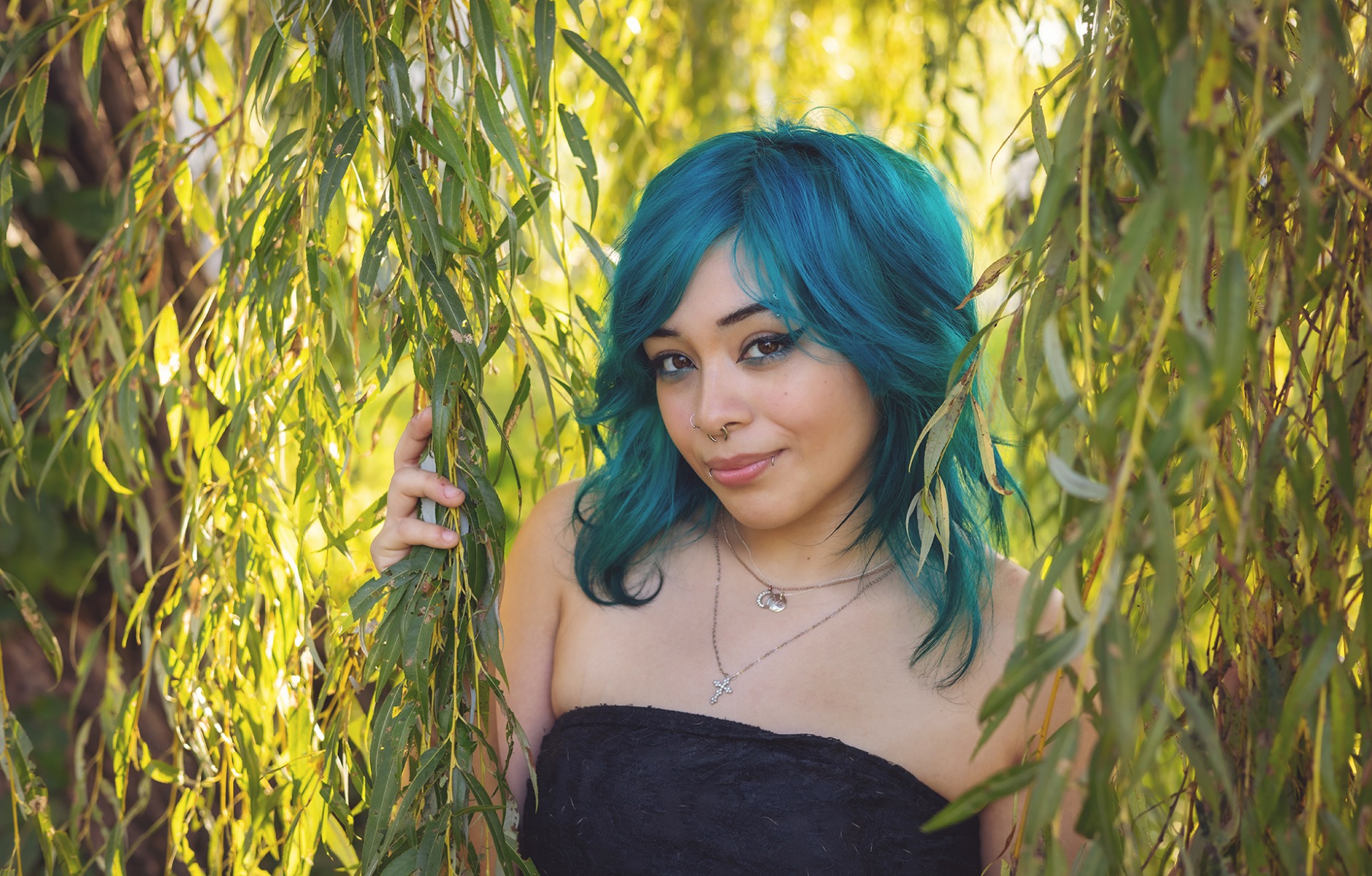 high school senior girl with teal blue hair poses amongst the branches of a willow tree