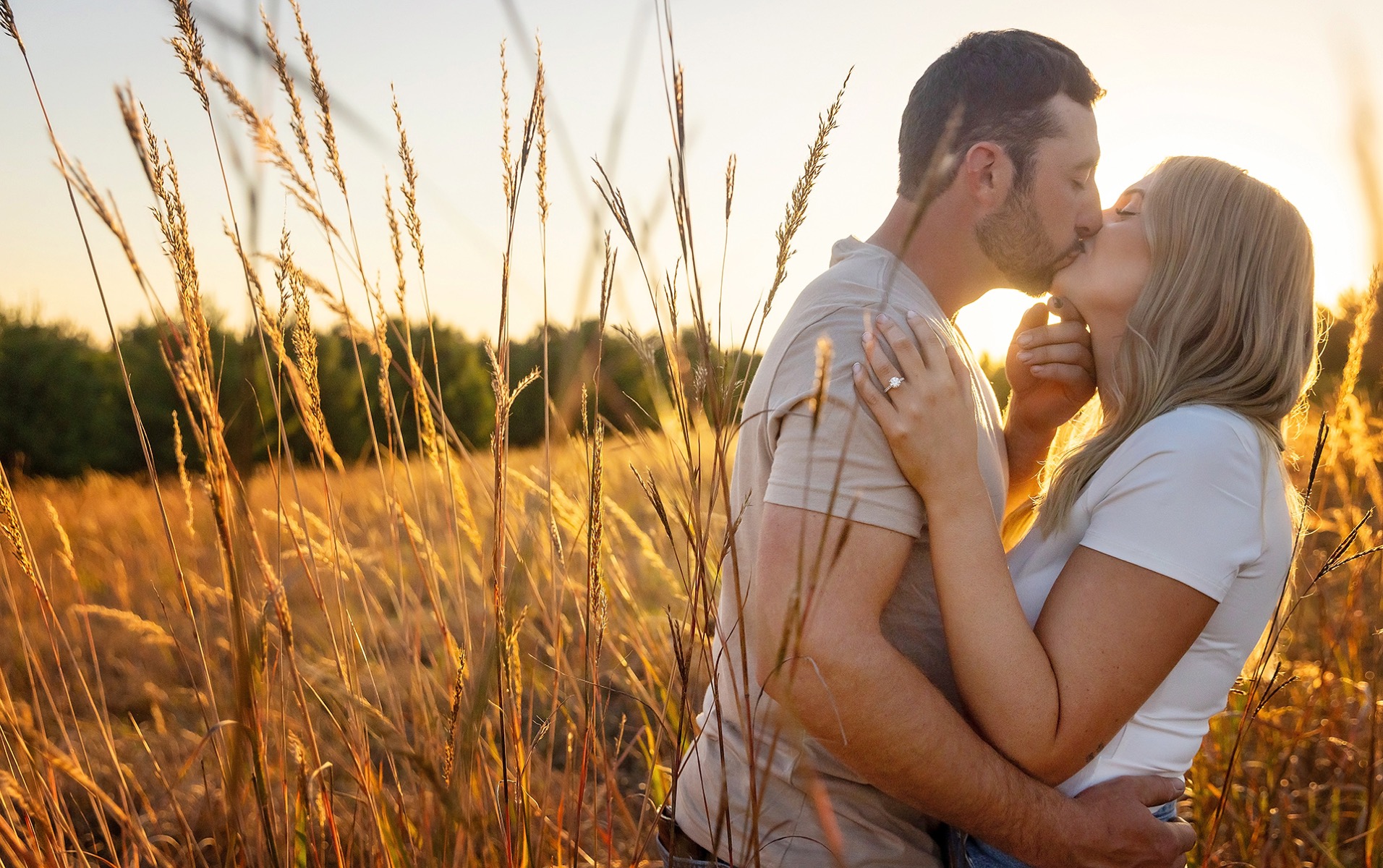 young engaged couple kisses in a field of tall grasses