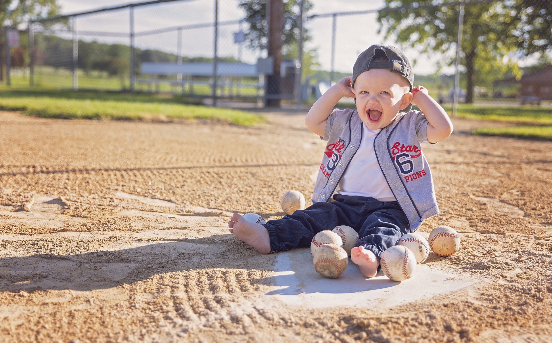 young toddler sits on home plate of a baseball field in his best baseball clothing