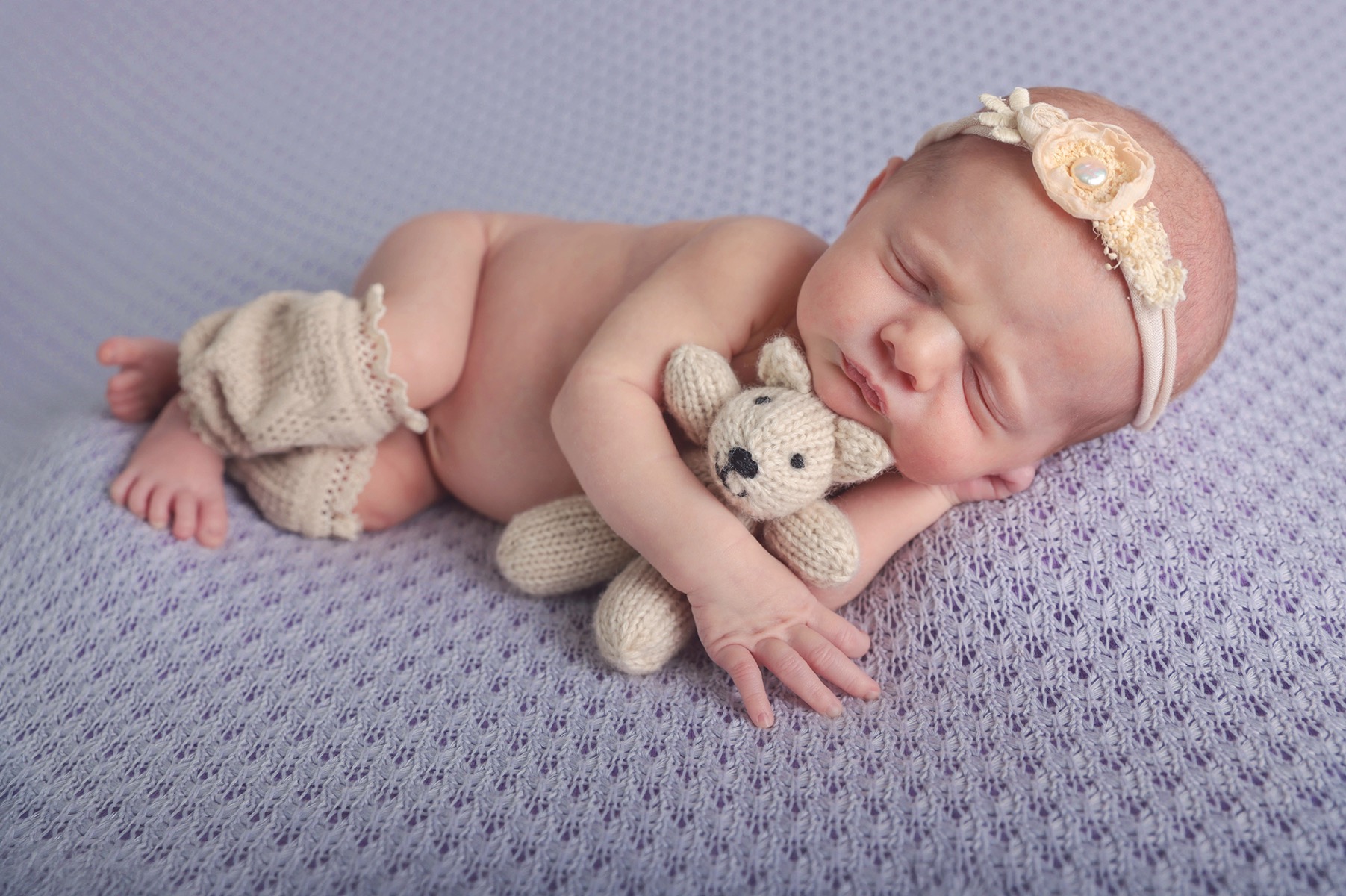 newborn baby girl laying on her side holding a small stuffed teddy bear 