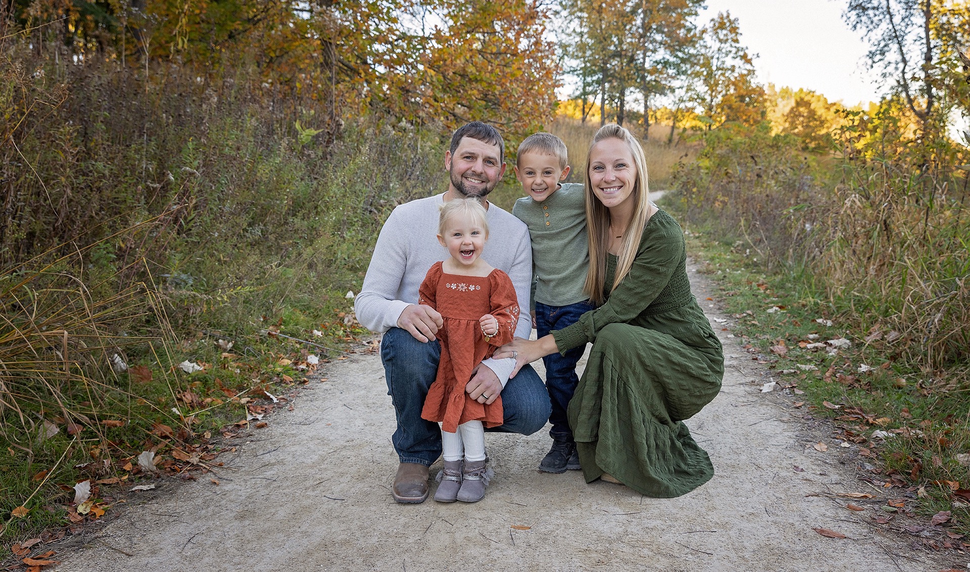 family of four crouches together on a pathway amongst the fall foliage